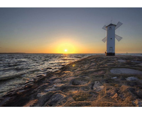 Zee en windmolen bij zonsondergang, weergegeven op een fotobehang met vuurtoren en rotsen.