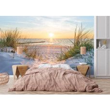 Fotobehang van een zonsondergang boven een strand, zee en duinen, met warme en rustgevende kleuren in een slaapkamer.