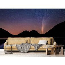 Een fotobehang van een sterrenhemel boven bergen en een meer in een woonkamer met vliesbehang.
