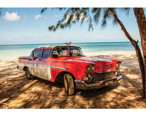 Fotobehang met een klassieke Cubaanse auto die langs een strand met palmbomen en een azuurblauwe zee rijdt, ideaal voor een vintage uitstraling.