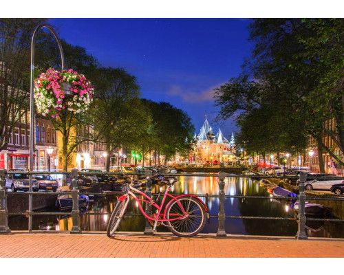 Fotobehang met rode fiets op een Amsterdams bruggetje bij avond, omringd door verlichte grachtenpanden en stille grachten.