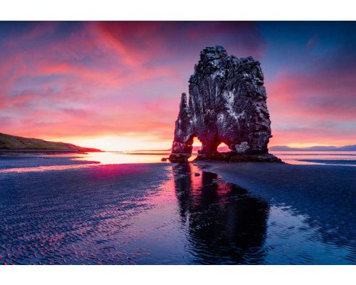 Fotobehang van Hvitserkur bij zonsondergang in IJsland, met de zee en de iconische drakenrots in beeld.