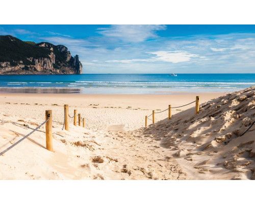 Fotobehang met strand en zeezicht, helderblauwe zee met een warme zon aan de horizon.
