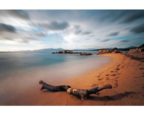 Fotobehang van een time-lapse opname van een strand, waar de oceaangolven het zand overspoelen in een serene setting.