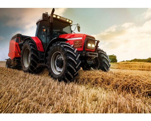 Fotobehang tractor op het land; een krachtige tractor maakt strobalen op een akker.