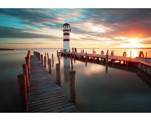 Fotobehang van een zonsondergang bij een vuurtoren aan de kust, met een prachtig uitzicht over de zee en natuur.