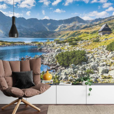 Een fotobehang met een bergmeer en helderblauw water omringd door bergen in een huiskamer.
