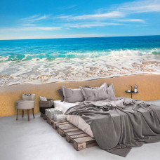 Een fotobehang met een blauwe zee en een tropisch strand, perfect voor een slaapkamer.