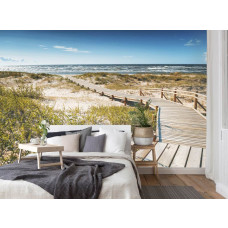 Een fotobehang van een brug door de duinen met uitzicht op het strand en de zee in vliesbehangstijl voor een slaapkamer.