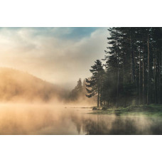 Fotobehang van mist die boven een meer hangt, omringd door bergen en bossen, met een serene en rustige sfeer.
