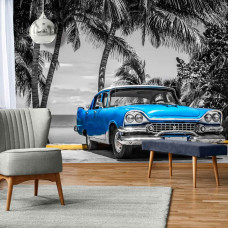 Fotobehang van een oude blauwe auto met palmbomen en de zee in Cuba, geschikt voor de huiskamer.