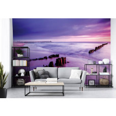 Een fotobehang met een strand en de zee met paarse tinten tijdens zonsondergang.