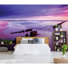 Een fotobehang met een strand en paarse lucht bij zonsondergang, geplaatst in een slaapkamer.