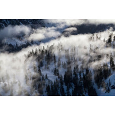 Fotobehang van een winterwonderland met besneeuwde bergen, waar een dichte mist het landschap een magische sfeer geeft.