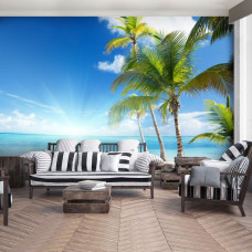 Een fotobehang met een zonnig strand met zee, zon en palmbomen, zichtbaar in een huiskamer.
