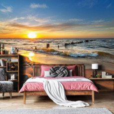 Een fotobehang met een natuurlijke zonsondergang boven een strandlandschap, passend bij een slaapkamer.
