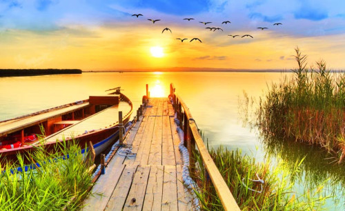 Fotobehang van een zonsondergang boven een pier die uitsteekt over een meer, omringd door een rustig natuurlandschap.