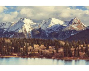 Fotobehang van imposante bergtoppen omgeven door dichte bossen en een helderblauwe lucht.