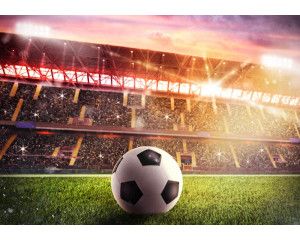 Fotobehang van een groot voetbalstadion met volle tribunes en een weids zicht op het veld, waar een wedstrijd in volle gang is.