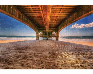 Uitzicht onder een pier die uitstrekt over een kalme zee, met de zonsondergang in de verte, fotobehang voor een serene en rustgevende sfeer.