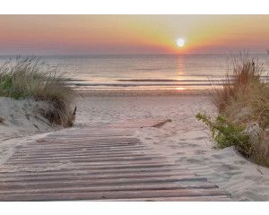 Fotobehang Romantische Zonsondergang aan het Strand, met een houten strandpad dat door de duinen naar de zee leidt, terwijl de zon in de horizon ondergaat.