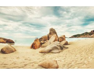 Fotobehang van rotsen op het strand die zich uitstrekken naar de zee, met een rustig en vredig landschap op de achtergrond.