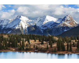 Fotobehang van bergtoppen bedekt met sneeuw boven een dicht bebost gebied, vastgelegd in een prachtig natuurlandschap.