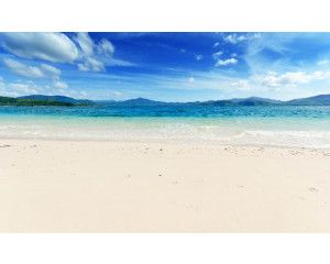 Fotobehang van een helderblauwe zee die tegen het strand aan spoelt, met een helderblauwe lucht op de achtergrond.