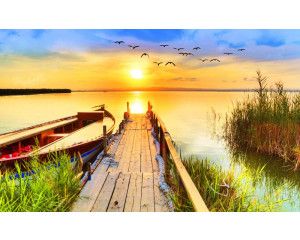 Fotobehang van een zonsondergang boven een pier die uitsteekt over een meer, omringd door een rustig natuurlandschap.